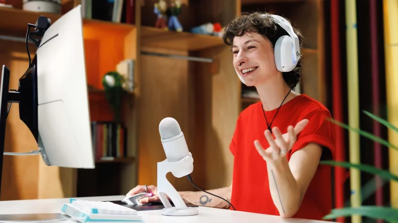 A streamer in white headphones talks into a white Logitech G Yeti 2 on a desk